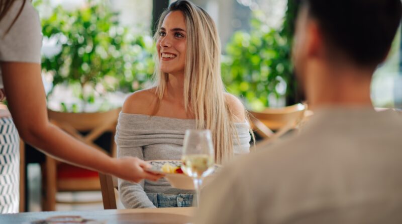 Smiling woman receiving food from waitress in restaurant