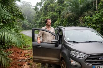 Homme à côté d'une voiture de location SUV au bord d'une route en Guyane, entouré de végétation tropicale dense