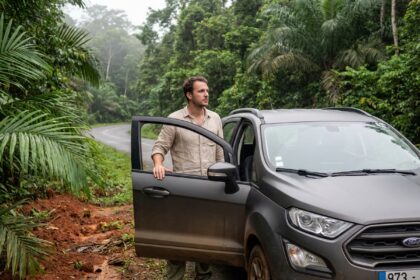 Homme à côté d'une voiture de location SUV au bord d'une route en Guyane, entouré de végétation tropicale dense